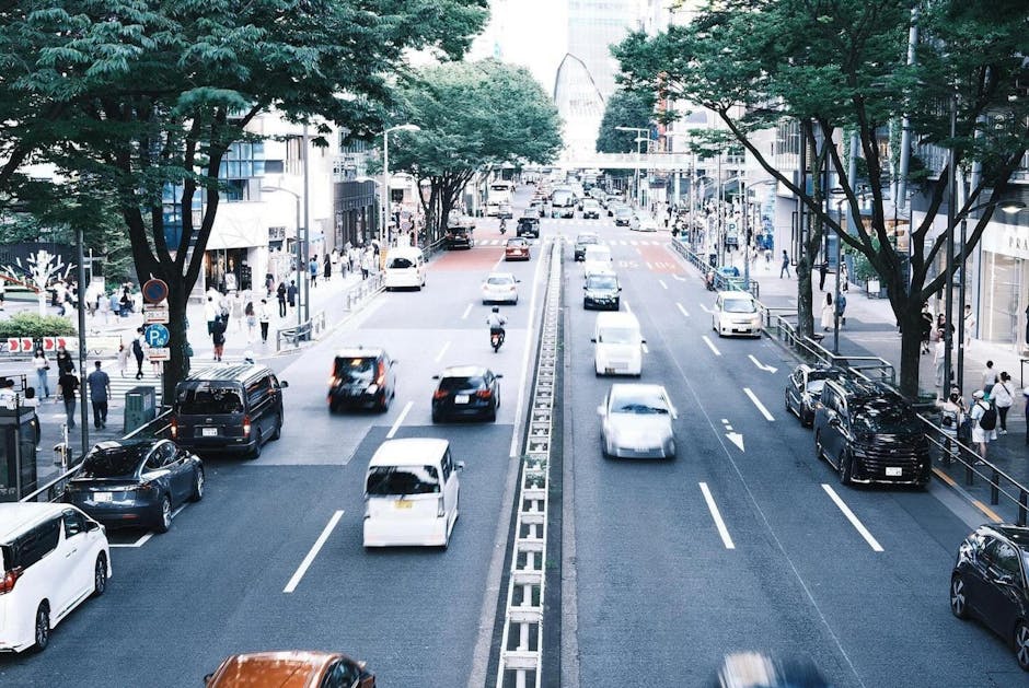 緑の木々の下、交通と歩行者が行き交う東京の賑やかな通りのダイナミックな風景。